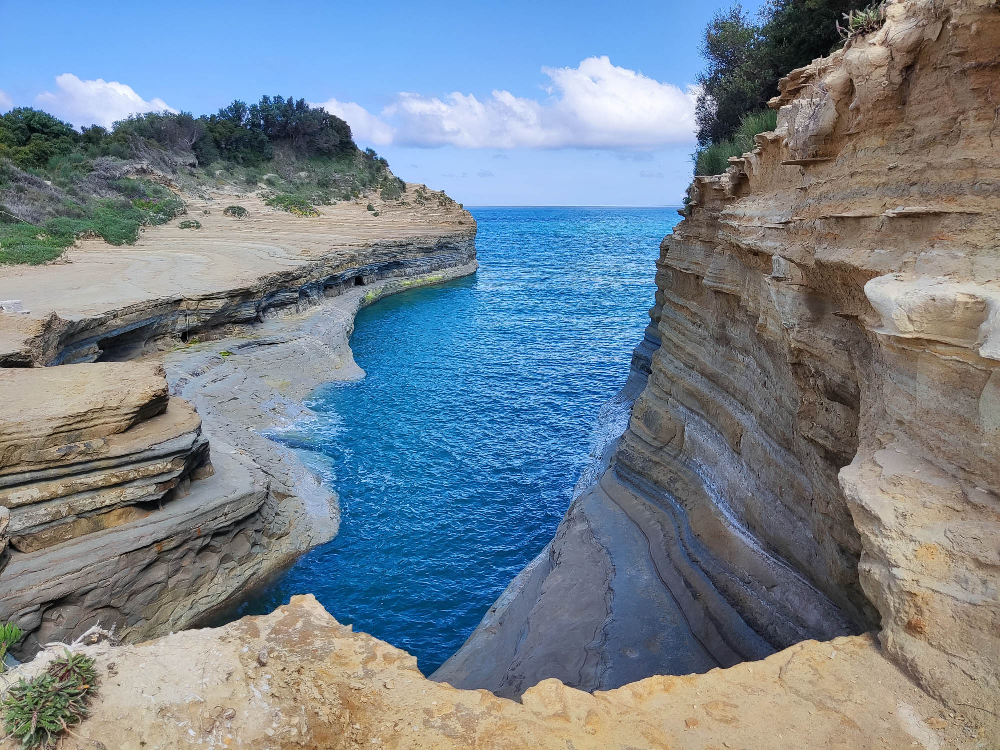 Kanał Miłości na Korfu z perspektywy skał od strony lądu. Przypominające sękacz skały piętrzą się nad wodą morską.
