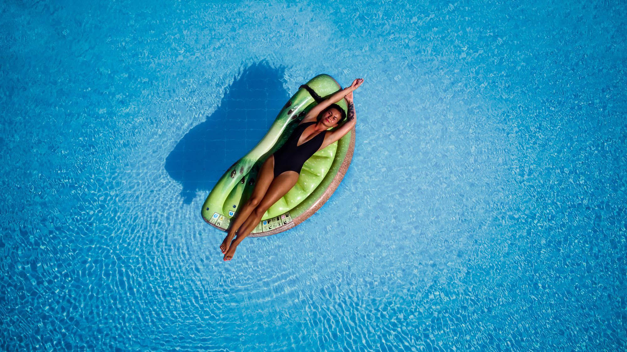 widok z loty ptaka na dziewczynę leżącą w basenie na materacu.