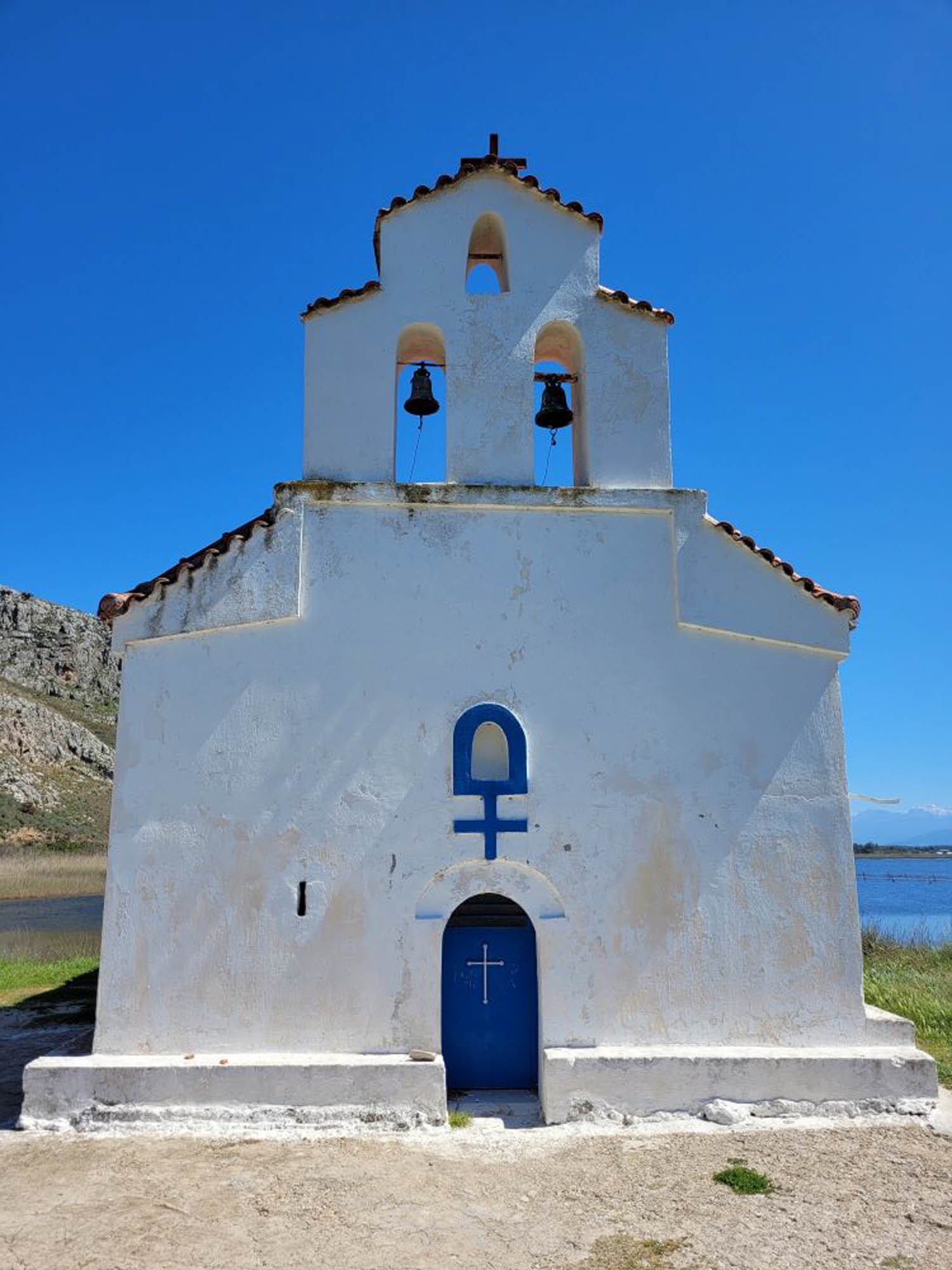 niebiesko-biała kapliczka, mała cerkiewka na brzegu, w tle niebieskie niebo i woda