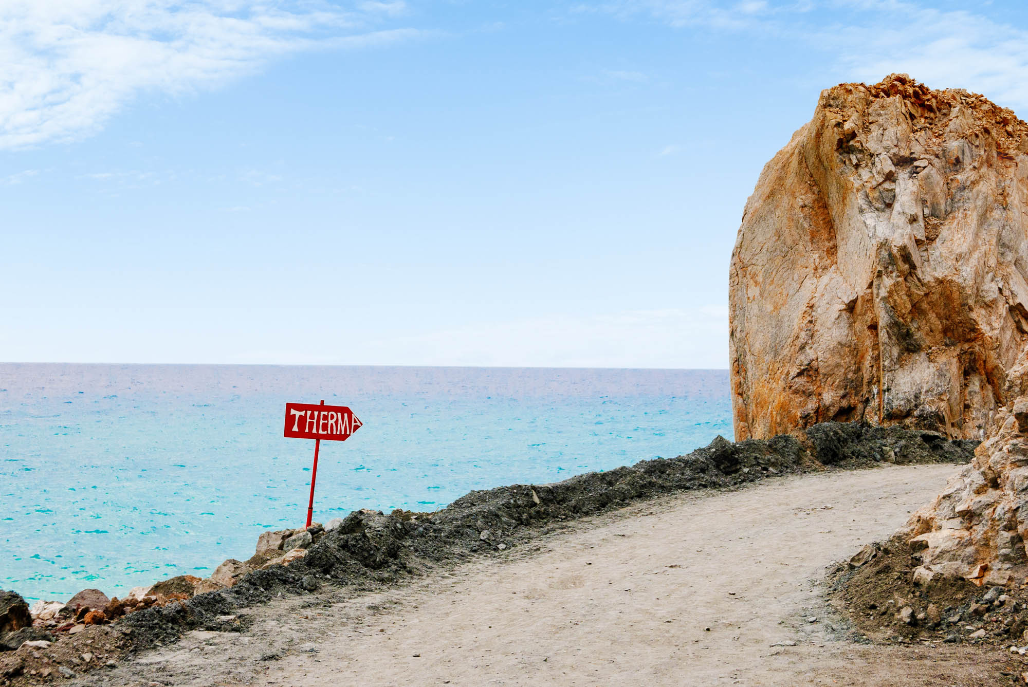 plaża, znak drogowy prowadzący na plaże piaszczystą ścieżką, niebo i skały