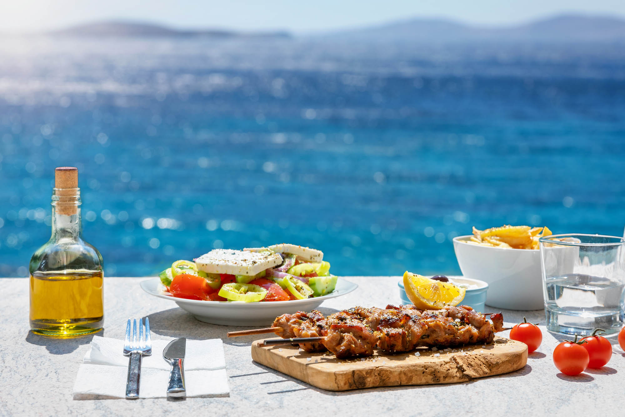 tradycyjny grecki stół, przekąski podane nad morzem, w tle błękitna woda i butelka oliwy