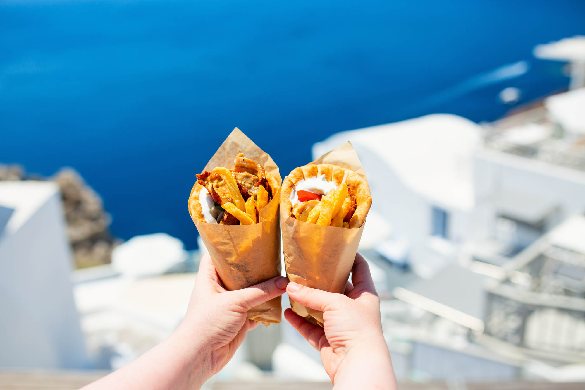 tyowa grecka pita z mięsem i frutkami, a w tle rajskie greckie miasto i morze, street food trzymany w dłoniach