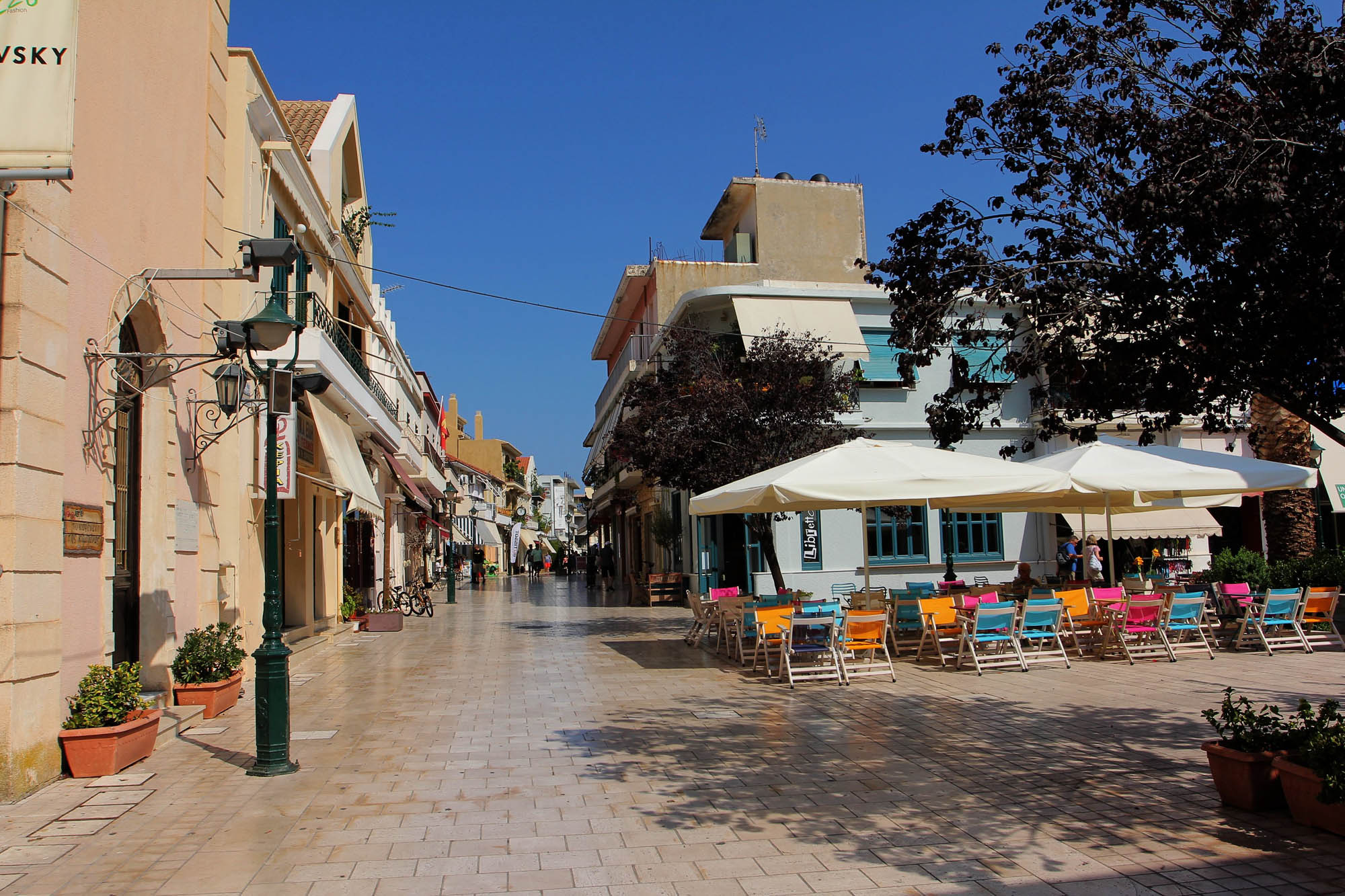 stolica wyspy Kefalonia, Argostoli, rozgrana słońcem ulica, deptak w mieście i parasolki w kafejce