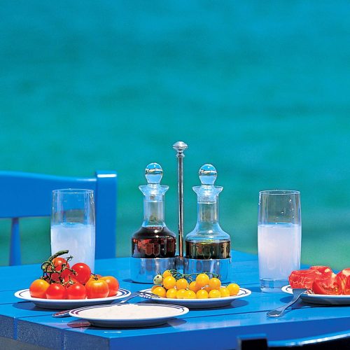 grecki, kolorowy stół z pomidorkami i przyprawami, kolorowe talerze i turkusowe morze w tle