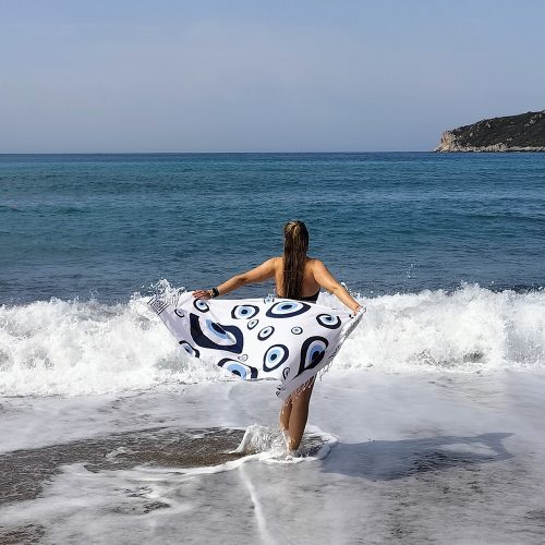 dziewczyna nad brzegiem morza trzyma pareo w charakterystyczny wzór z greckim, niebieskim okiem