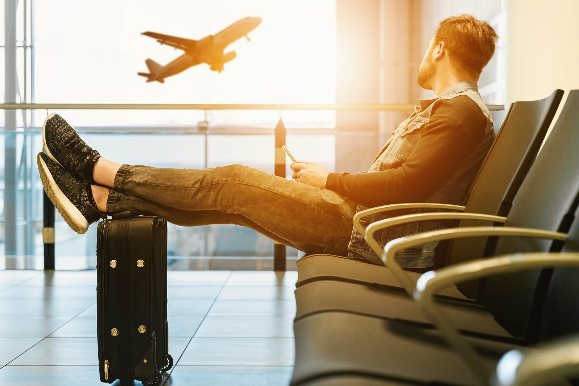 człowiek siedzący na lotnisku z bagażem, czekający na swój lot