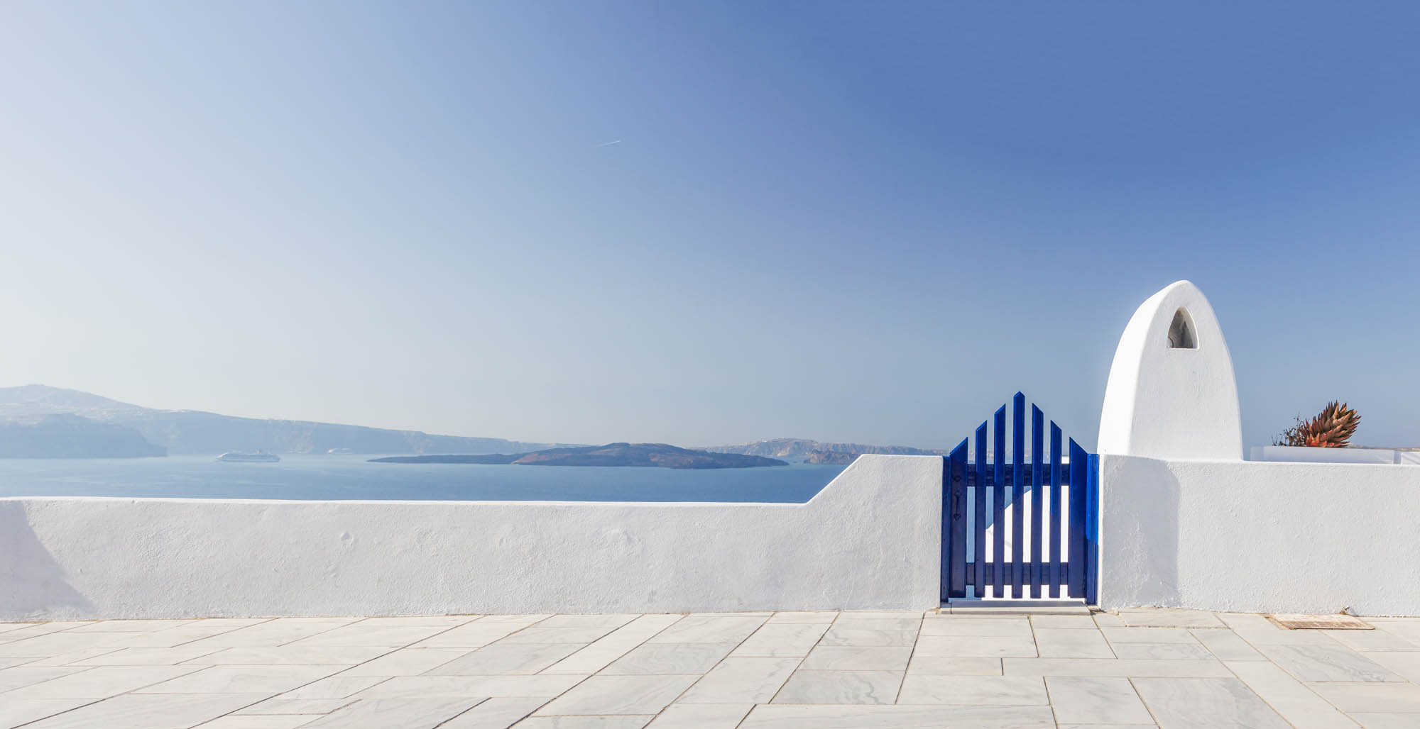 grecko, biały niebieski pejzaż z niebem w tle, biały budynek i niebieska furtka