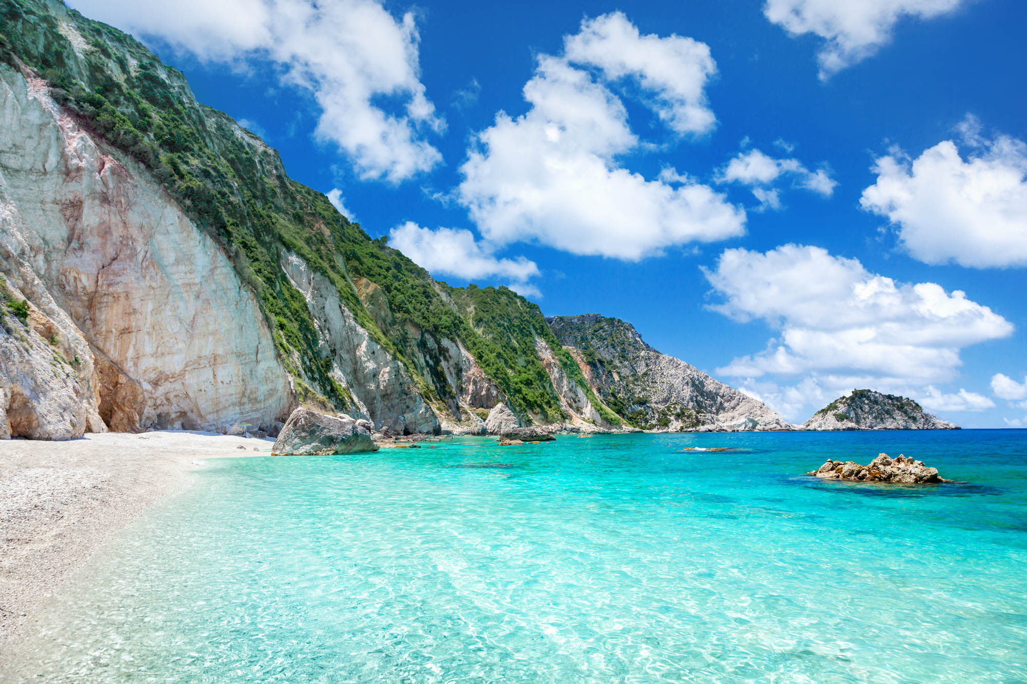 widok na piękną grecką plaże z lazurową wodą, niebo z chmurkami i biały piasek