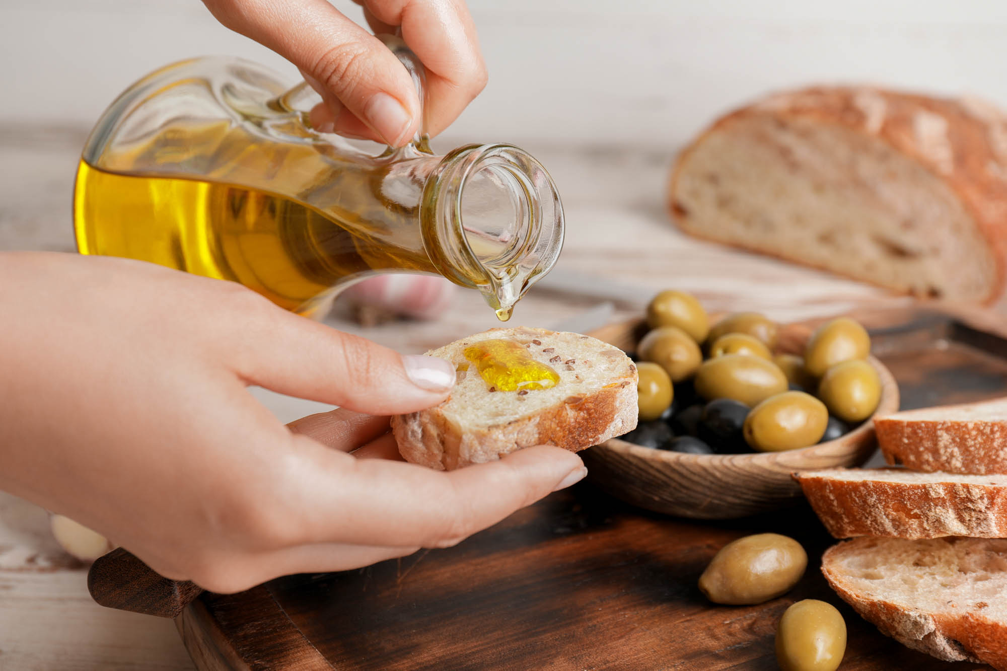 oliwa z oliwek z chlebem, osoba oblewa chlebek oliwą, obok w misce oliwki