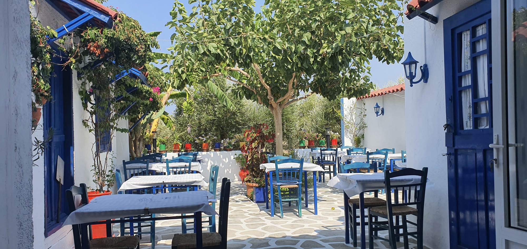 typowa grecjka ulica ze stolikami i krzesłami, biało niebieskie tawerny