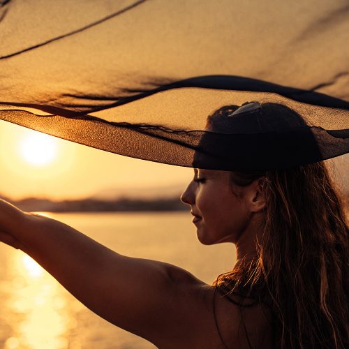 kobieta trzyma pareo nad głową i patrzy na zachód słońca