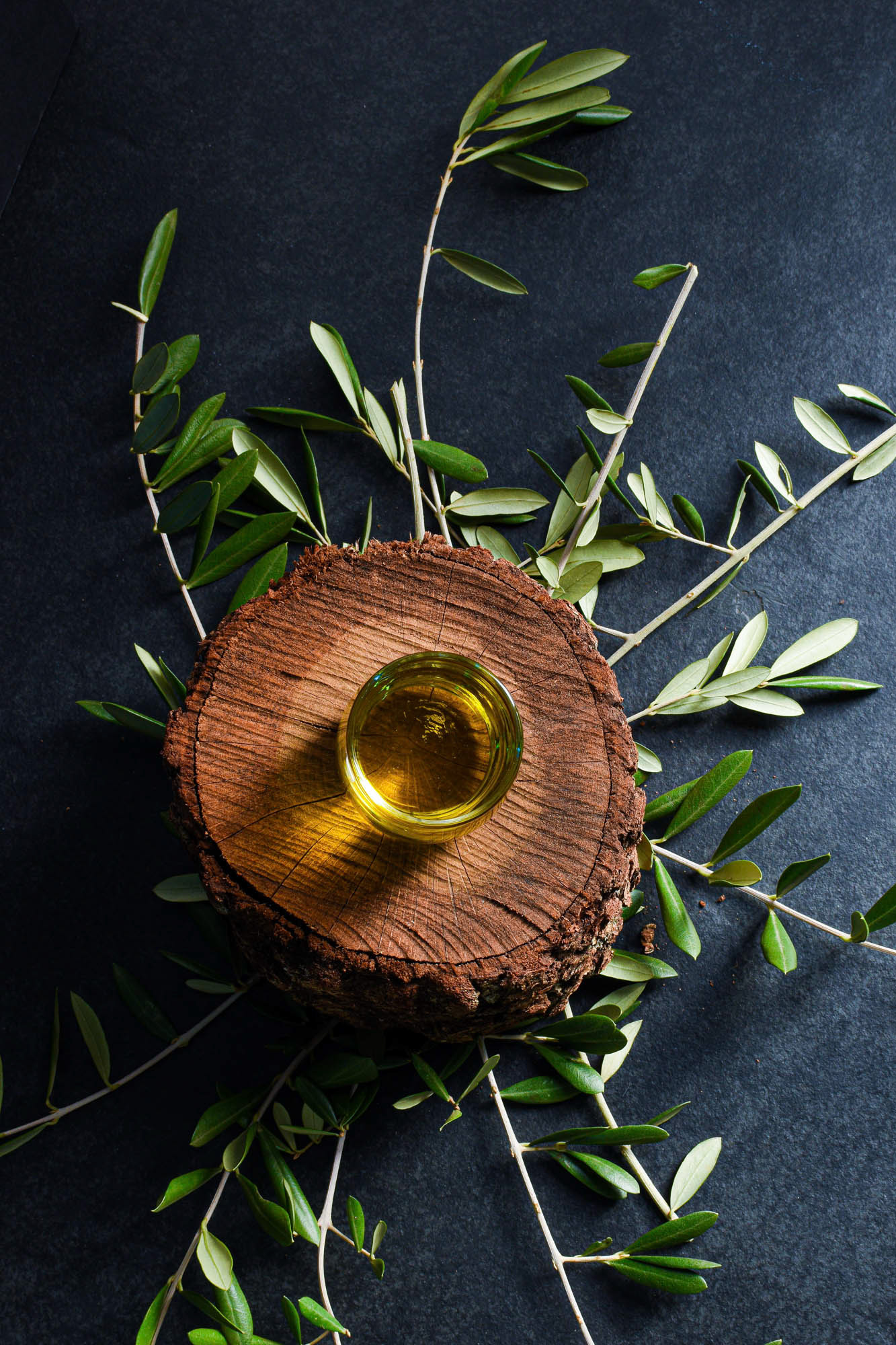 oliwa z oliwek w przezroczystym naczyniu, na drewnianej desce z gałązkami oliwnymi