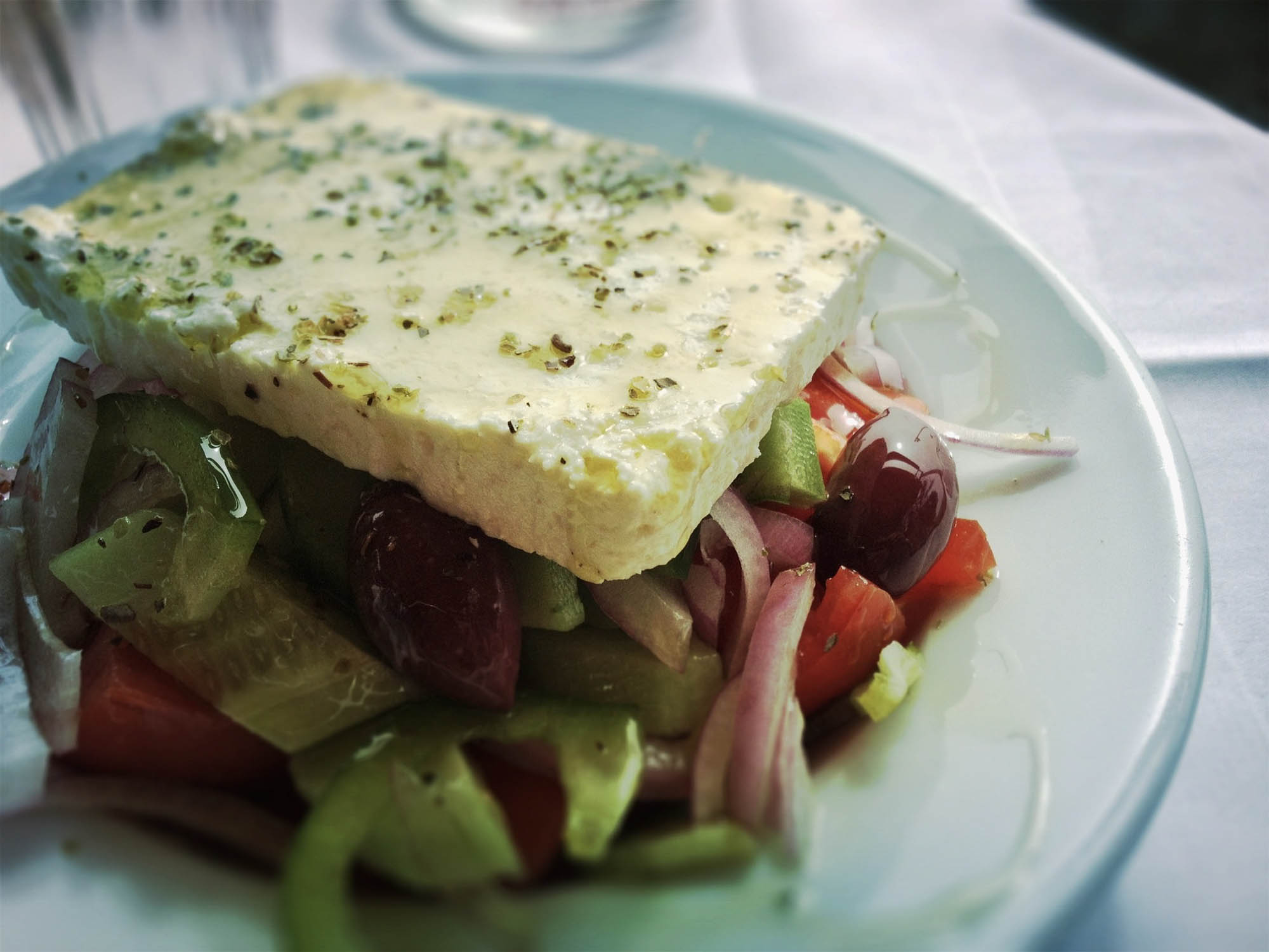 grecka sałatka z dużym kawałkiem sera feta na wierzchu, oliwa z oliwek, detal na talerzu