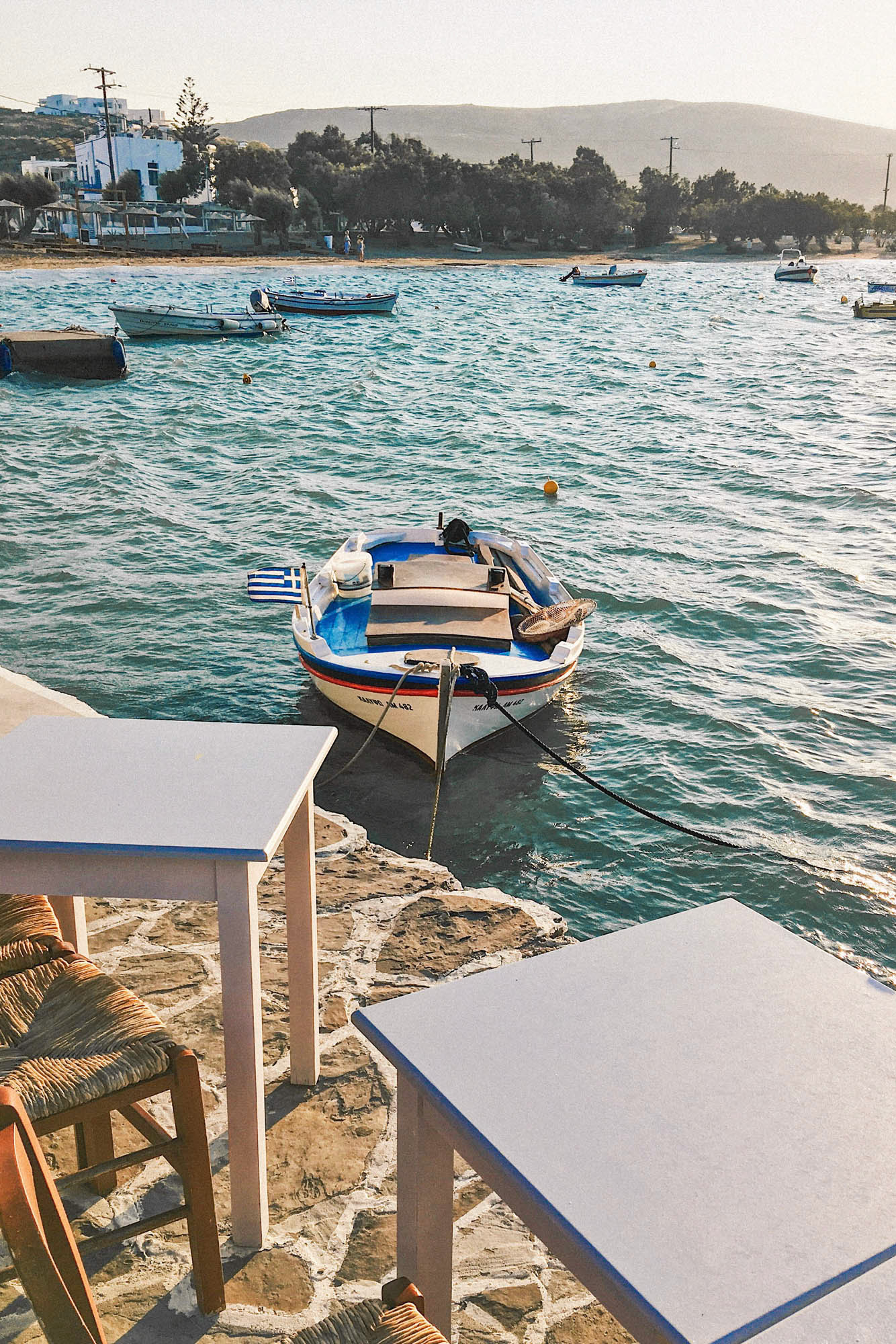 widok na łódkę kołyszącą się przy przystani ze stolikami, w tle morze