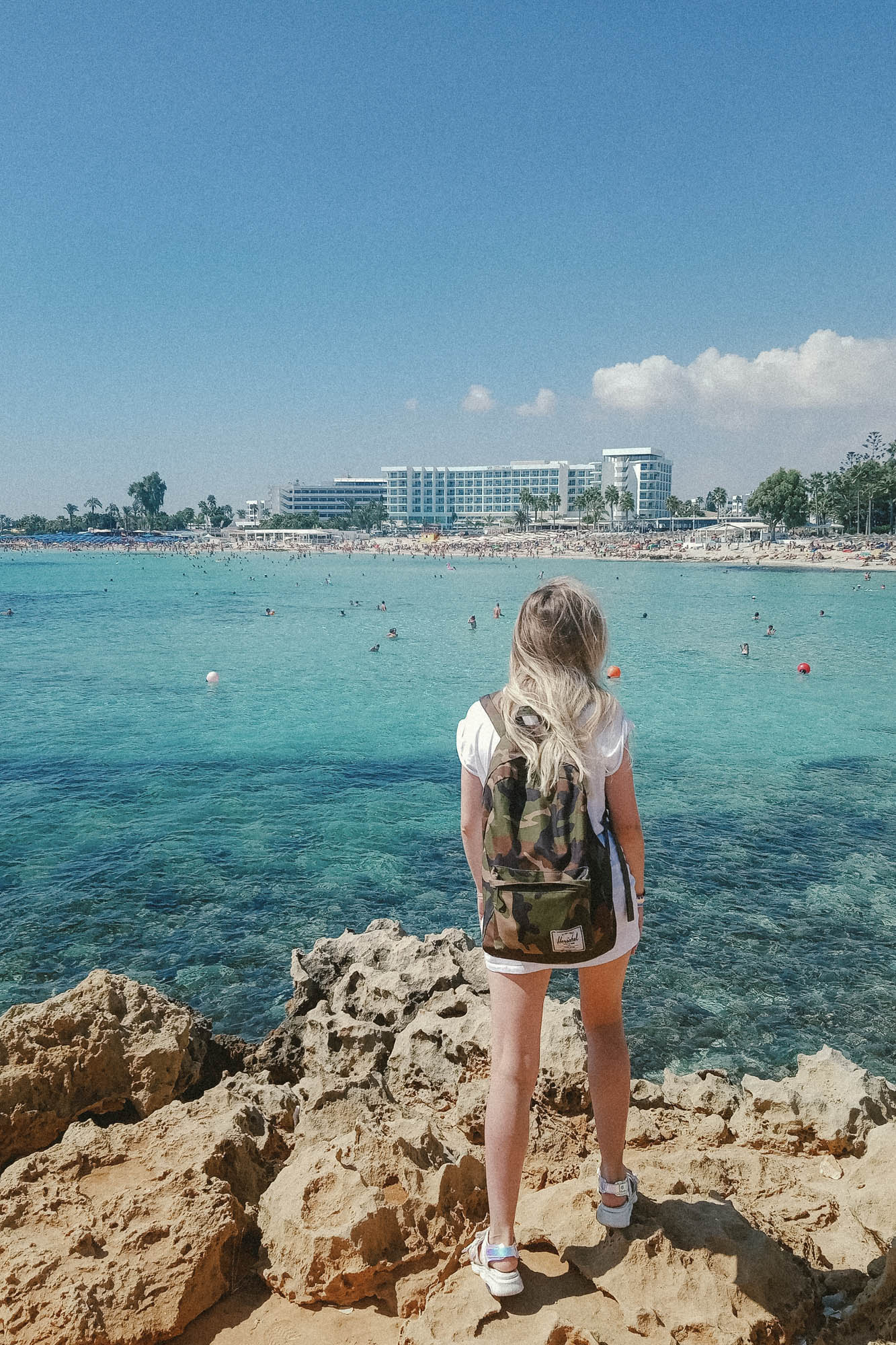 widok na wybrzeże w mieście larnaka, dziewczyna stojąca na skałach, na skalistym klifie , patrzy na lazurowe morze i hotele w oddali