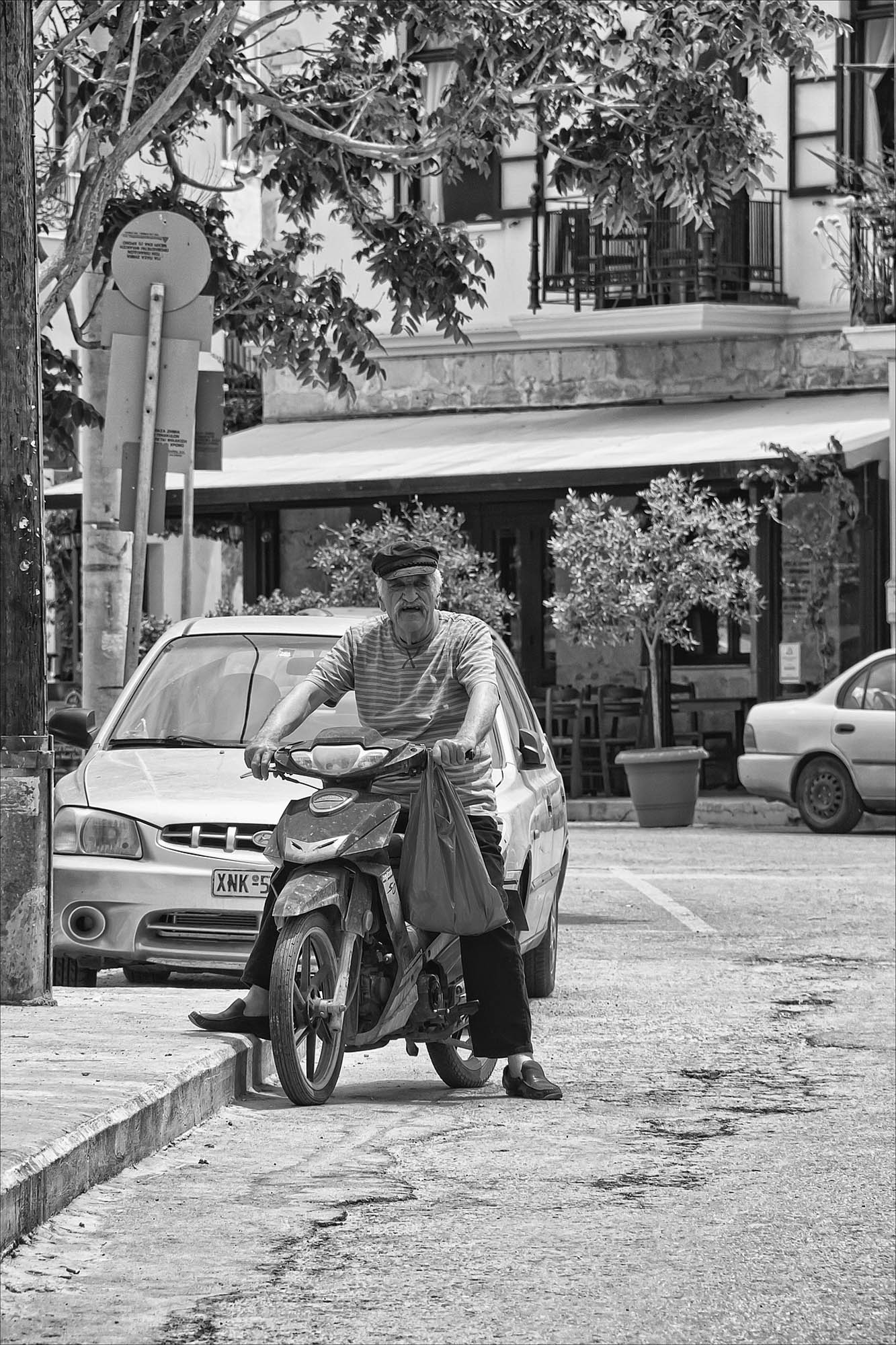 jedna z ulic miasta chania, na pierwszym planie grek prowadzi swój stary skuter
