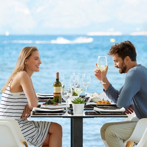para siedząca przy stoliku i pijąca wino na tle błękitnego morza