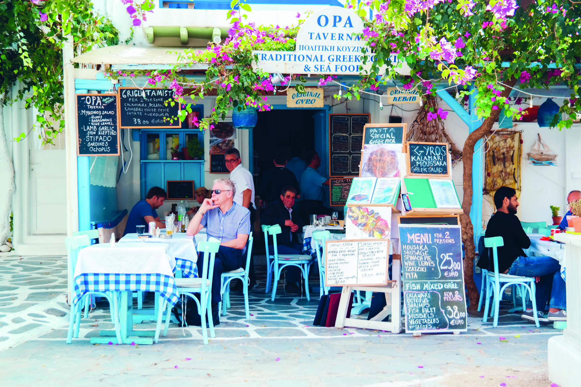 typowa grecka ulica, ludzie siedzą przy stolikach w greckim kafenionie