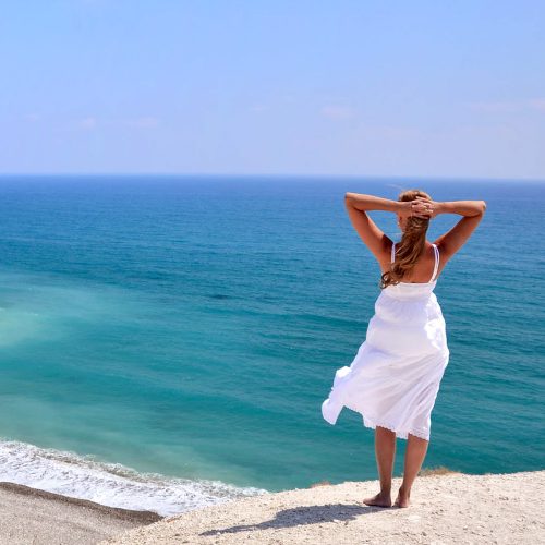 cypr, dziewczyna w białej sukience, stojąca na klifie , ponad brzegiem morza